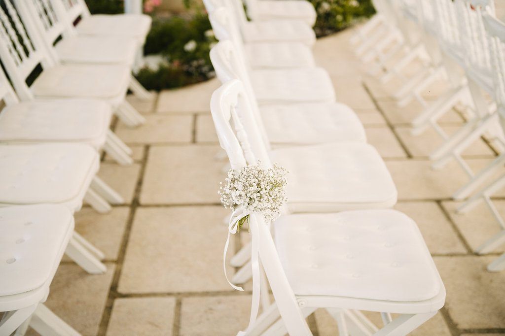 White wedding ceremony chairs decorated with delicate baby breath flowers and flowing white ribbon.