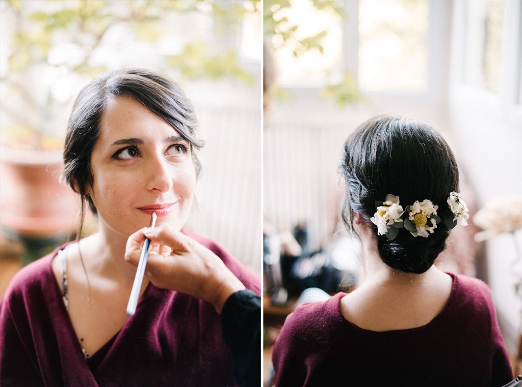 Bride with elegant floral updo hairstyle applying lip makeup before wedding ceremony.