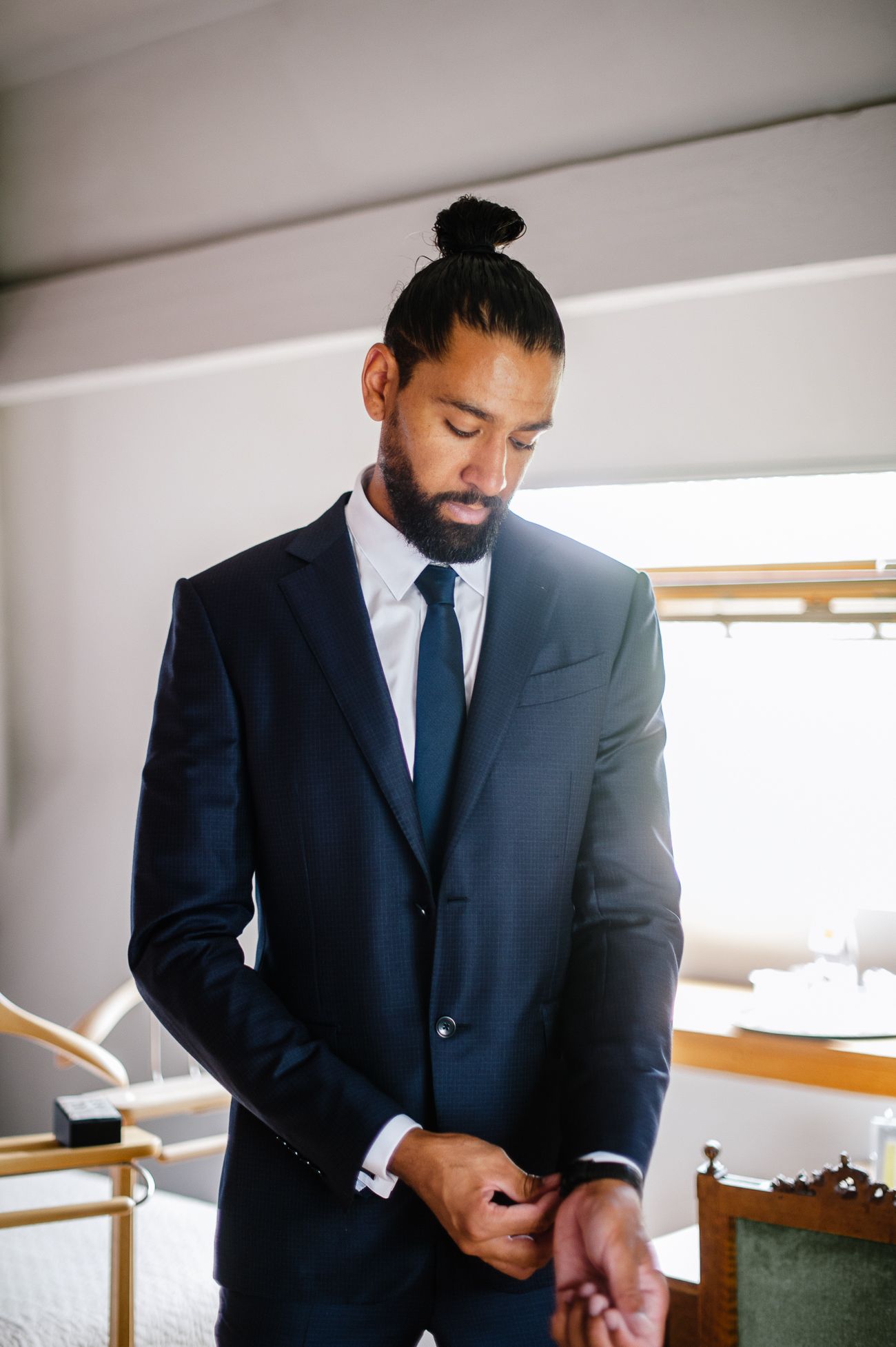 Groom in navy blue suit adjusting cufflinks before wedding ceremony.