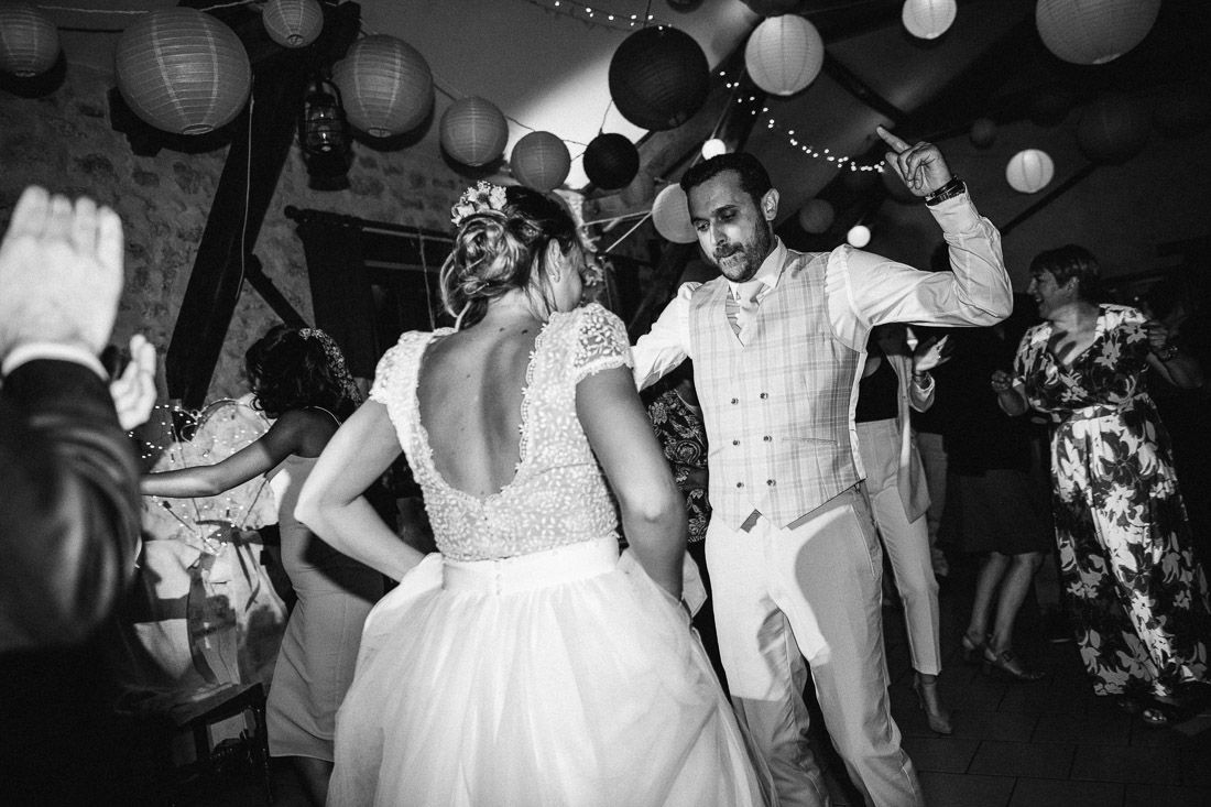 Bride and groom dance under paper lanterns at festive indoor wedding reception in black and white.