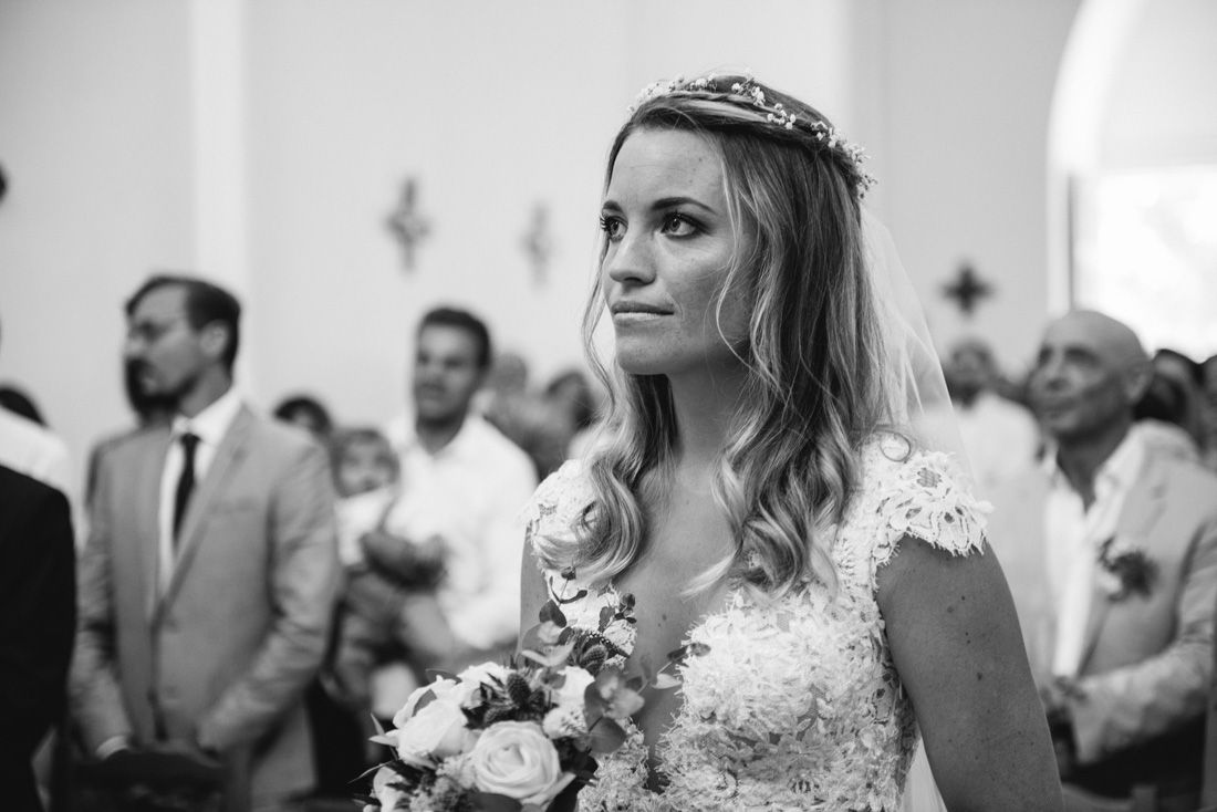 Emotional bride in lace wedding dress holding bouquet during church ceremony in black and white photo.