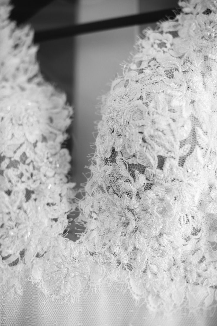 Close-up black and white photo of intricate floral lace wedding dress detail on hanger.