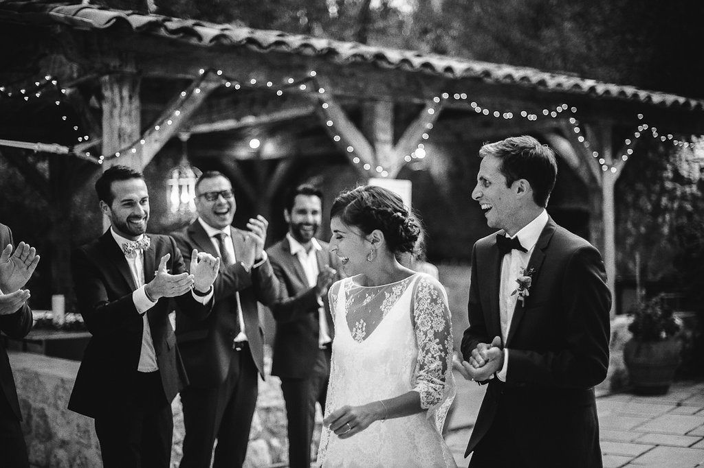 Black and white photo of bride and groom entering reception amid applauding guests.