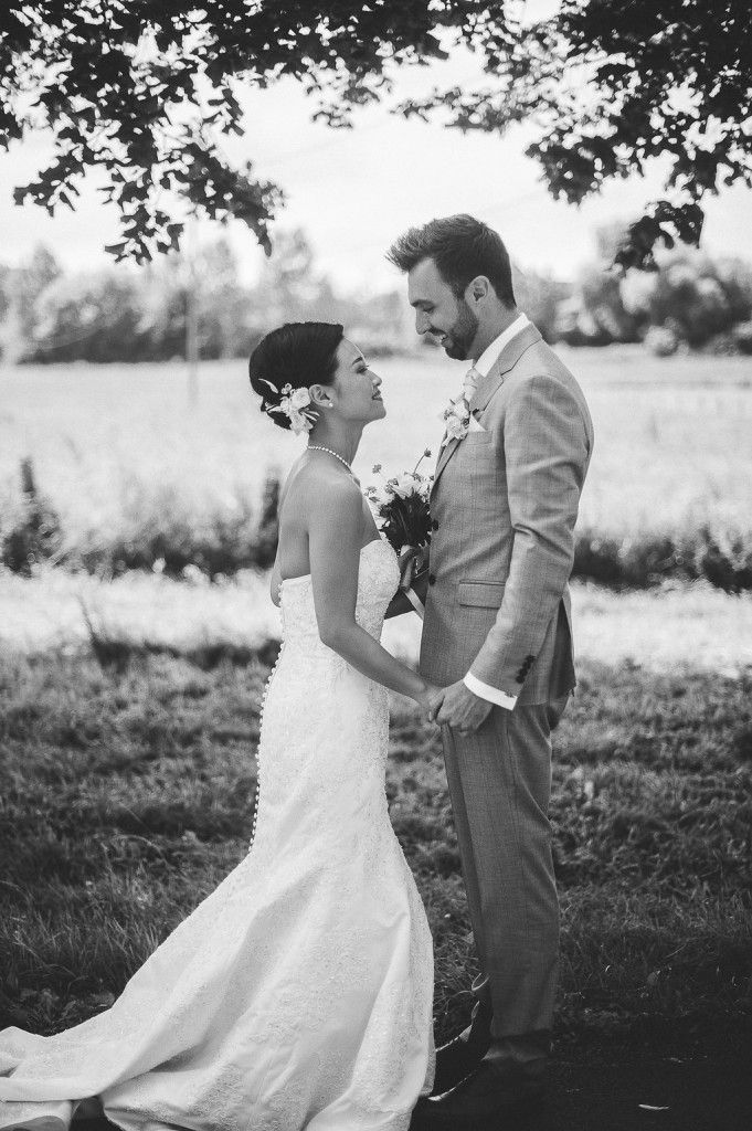 Black and white full-length portrait of a bride and groom holding hands and smiling under a shady tree.