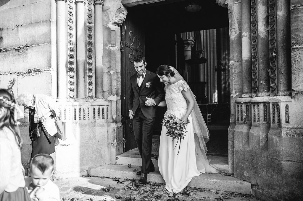Bride and groom descend stone church steps in an elegant black and white wedding photograph.