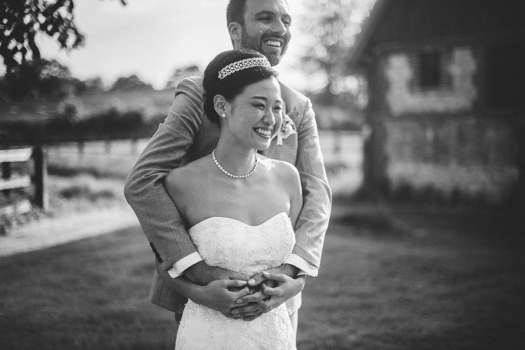 Black and white photo of a smiling bride and groom embracing outdoors on their wedding day.