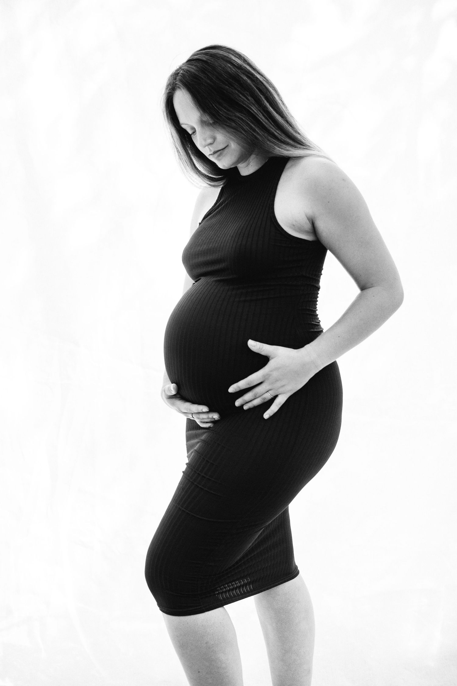 Black and white portrait of pregnant woman in black dress cradling her baby bump.