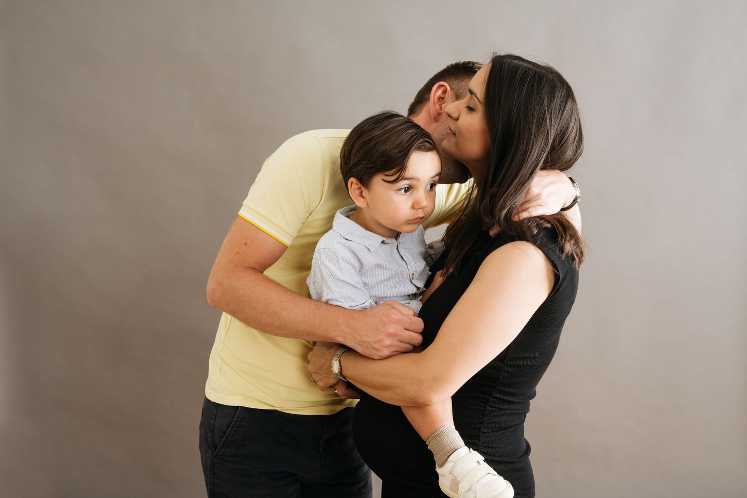 Parents kissing young boy on cheeks in studio portrait.