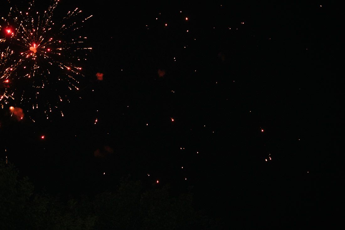 Red fireworks bursting against dark night sky during outdoor wedding celebration.