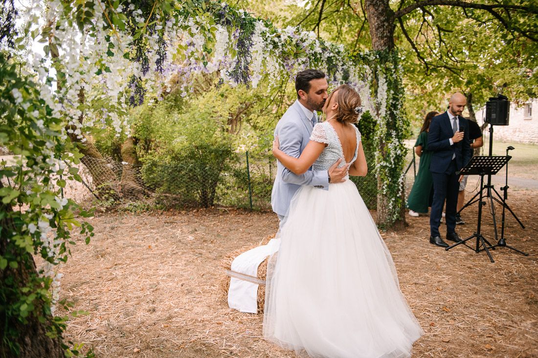 Bride and groom share first dance under wisteria blooms at elegant outdoor garden wedding reception.