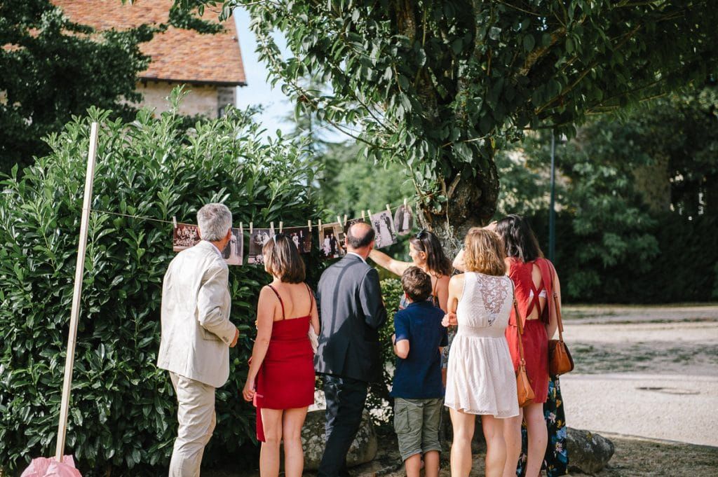 Wedding guests gather around an outdoor display of hanging decorations among lush green trees.
