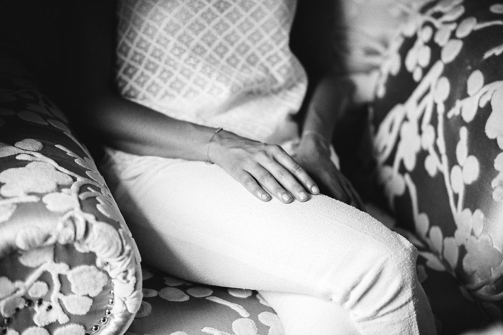 Black and white close-up of bride sitting on floral sofa wearing white pants.
