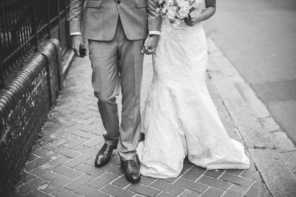 Black and white photo of a bride and groom walking hand in hand on a brick sidewalk on their wedding day.