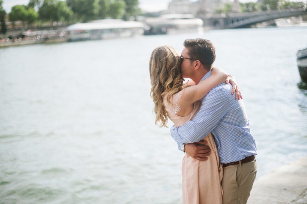 Couple sharing a kiss while embracing by the scenic Seine River in Paris.