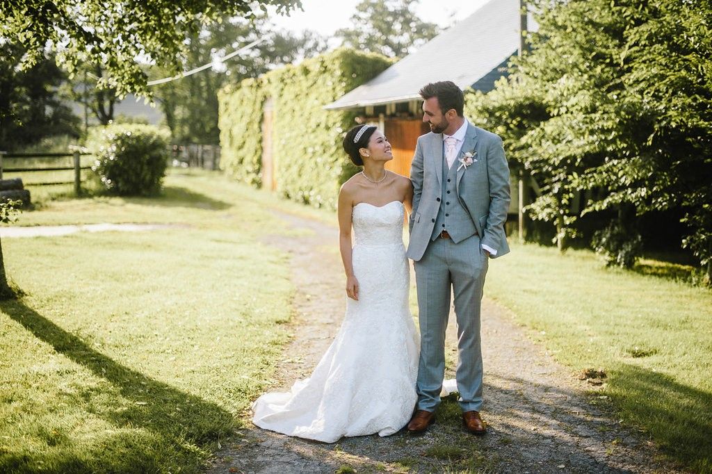 Bride in strapless lace gown and groom in grey suit share a tender moment in a garden.