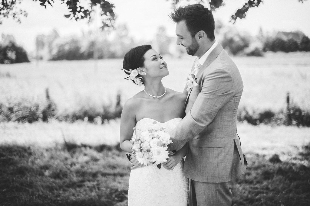 Black and white romantic portrait of a bride and groom embracing in an open field on their wedding day.
