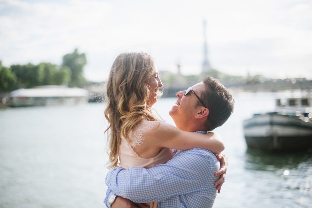 Couple embracing and smiling by the Seine River with the Eiffel Tower in the background in Paris.