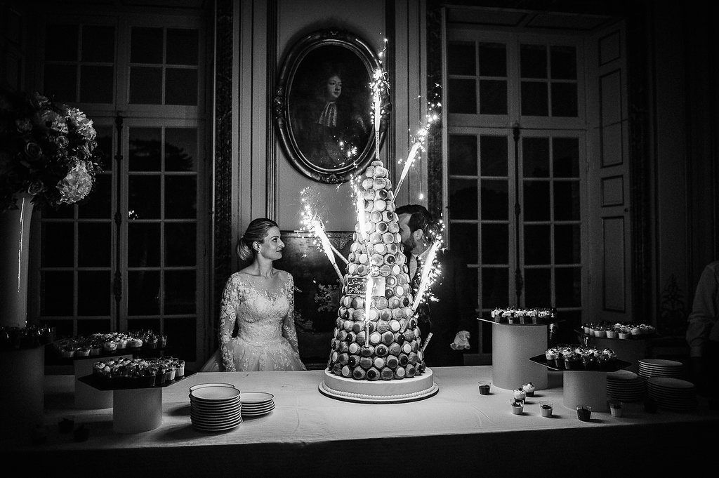 Black and white photo of couple beside sparkling croquembouche wedding cake tower at reception.