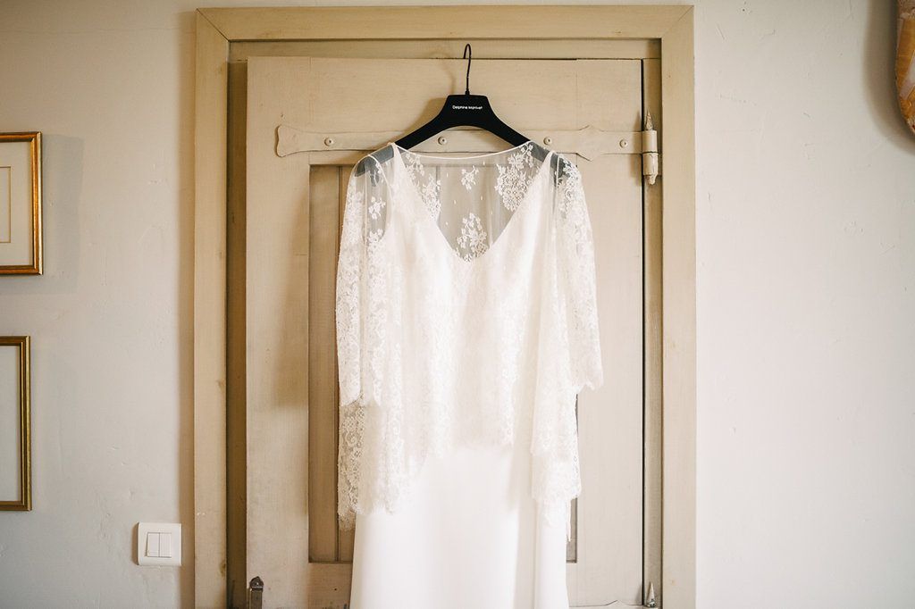 White lace wedding dress with long sleeves hanging on a wooden door frame.