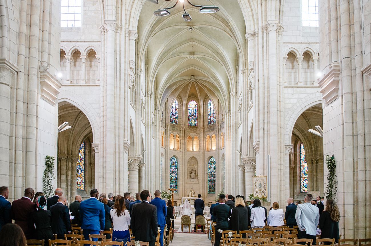 Elegant wedding ceremony inside a grand Gothic cathedral with vaulted arches, stained glass windows, and guests seated in wooden pews.
