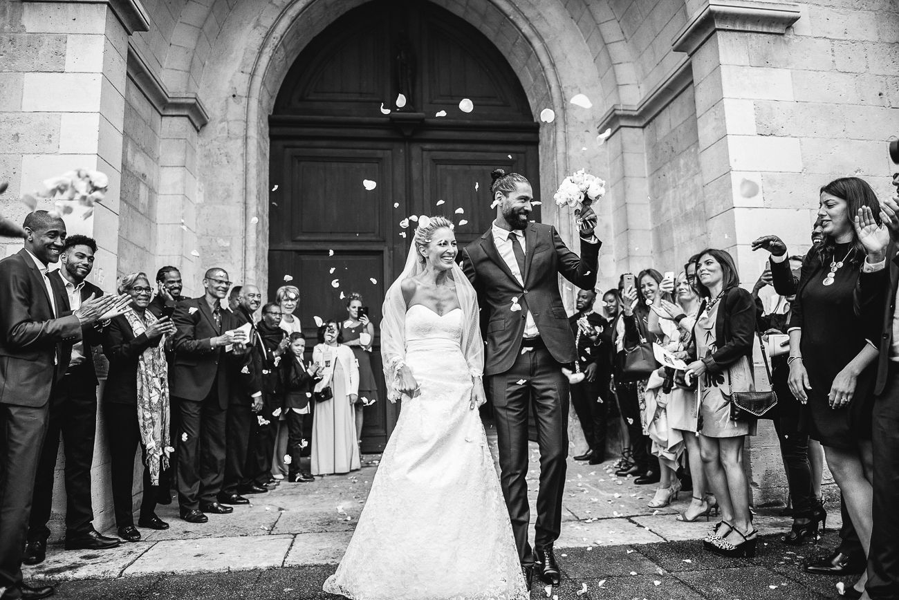 Black and white photo of a joyful bride and groom exiting a church as guests throw confetti at their wedding.