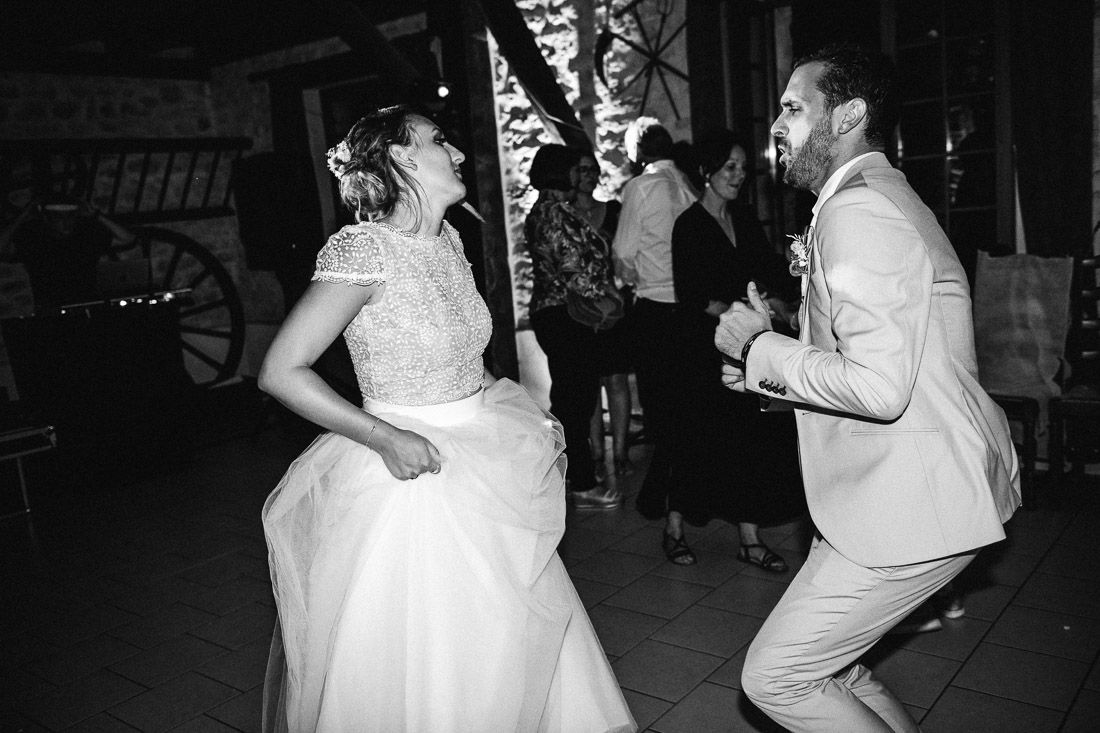 Bride and groom dance energetically together at outdoor wedding reception in black and white photo.
