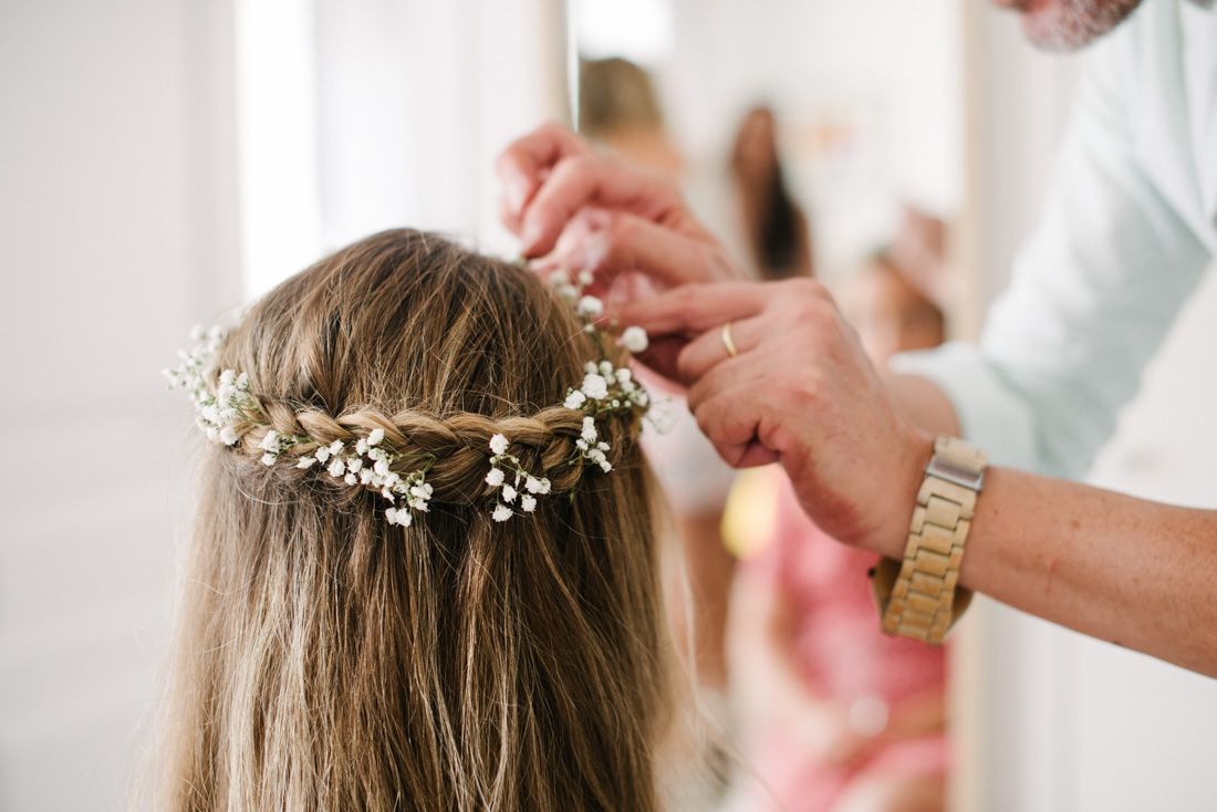 Hairstylist placing delicate baby's breath floral crown into bride's braided hair during wedding preparation.