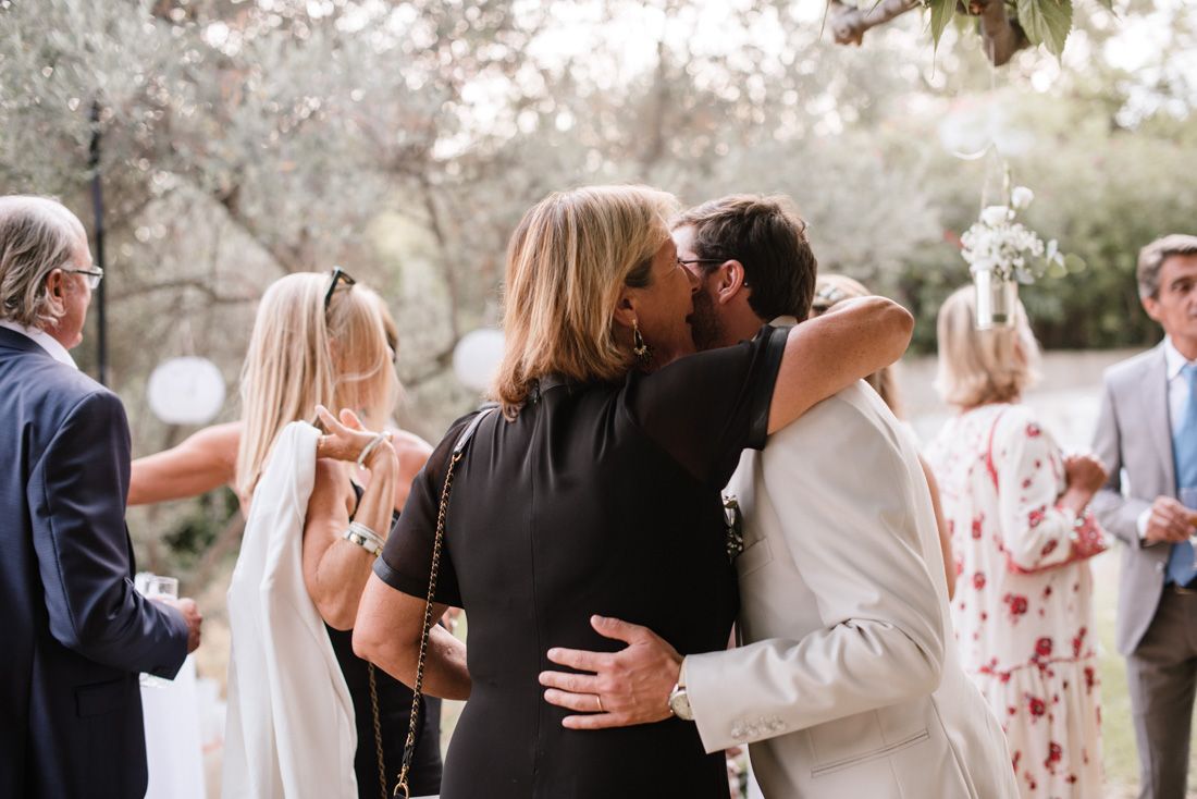 Wedding guests embracing and congratulating the groom in an outdoor ceremony setting.