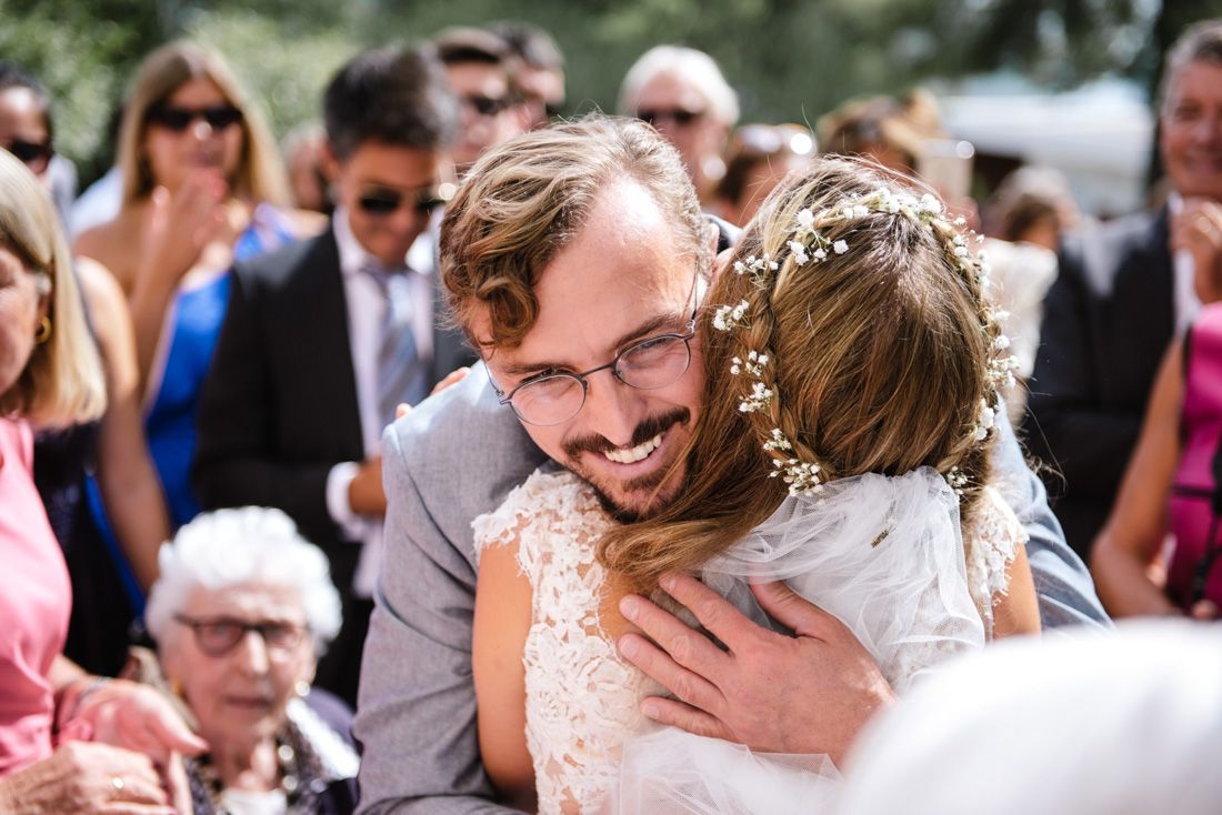 Bride and groom share a heartfelt hug during outdoor wedding ceremony, bride wearing floral crown.