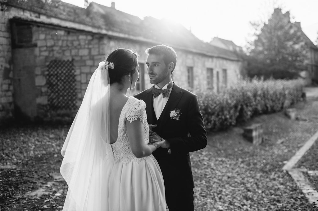 Black and white photo of bride and groom sharing an intimate moment outdoors near a stone building.