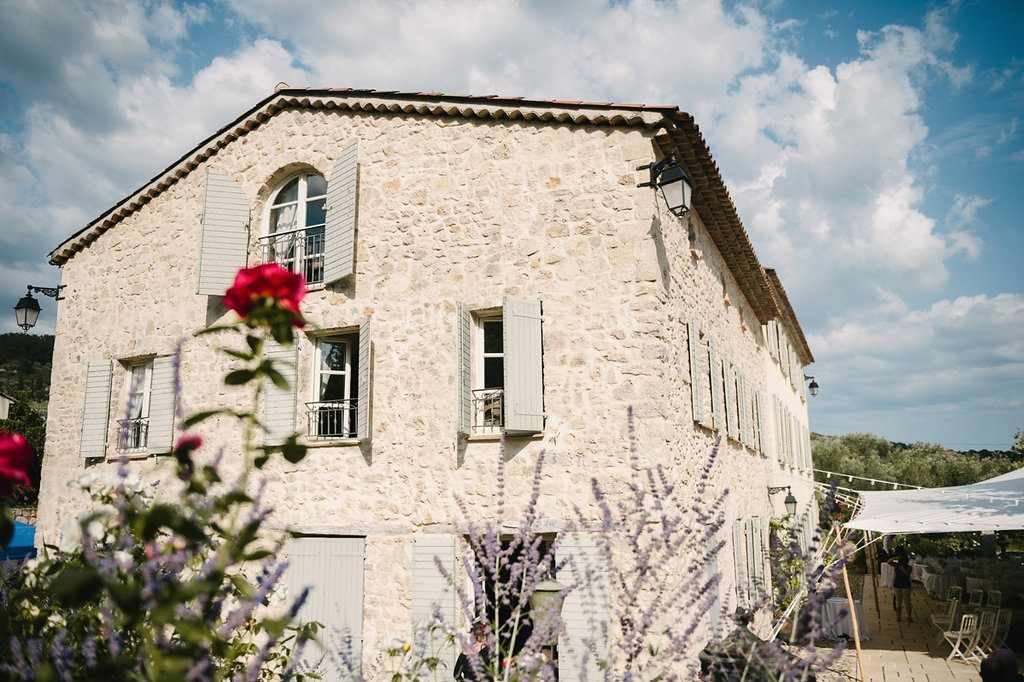 Rustic stone Provencal wedding venue exterior with red roses and lavender in foreground.