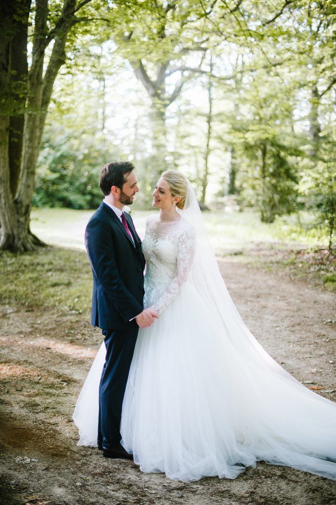 Bride and groom share a romantic moment on a woodland path, bride wearing a lace long-sleeve ballgown with veil.
