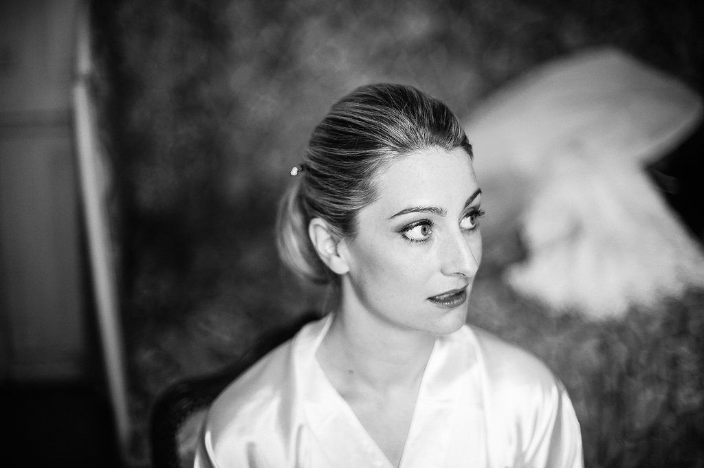 Black and white portrait of a bride in white robe with dramatic eye makeup and updo.