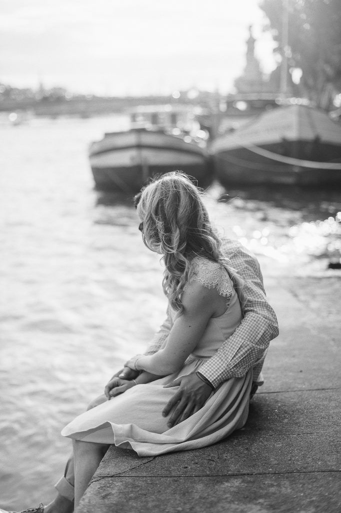 Black and white photo of a woman with flowing hair sitting by the Seine River in Paris.