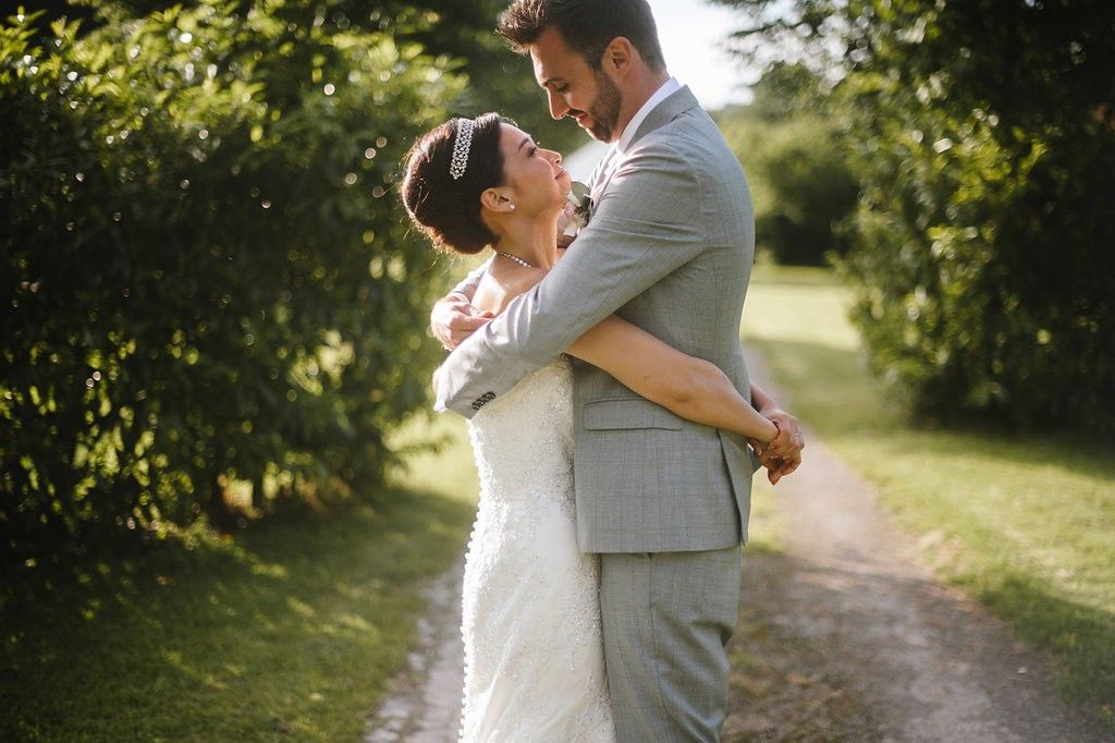 Smiling bride and groom embrace joyfully on scenic garden path surrounded by greenery.