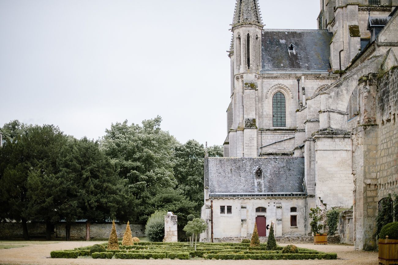 Historic French château garden with manicured hedges and ornate stone church architecture under overcast sky.