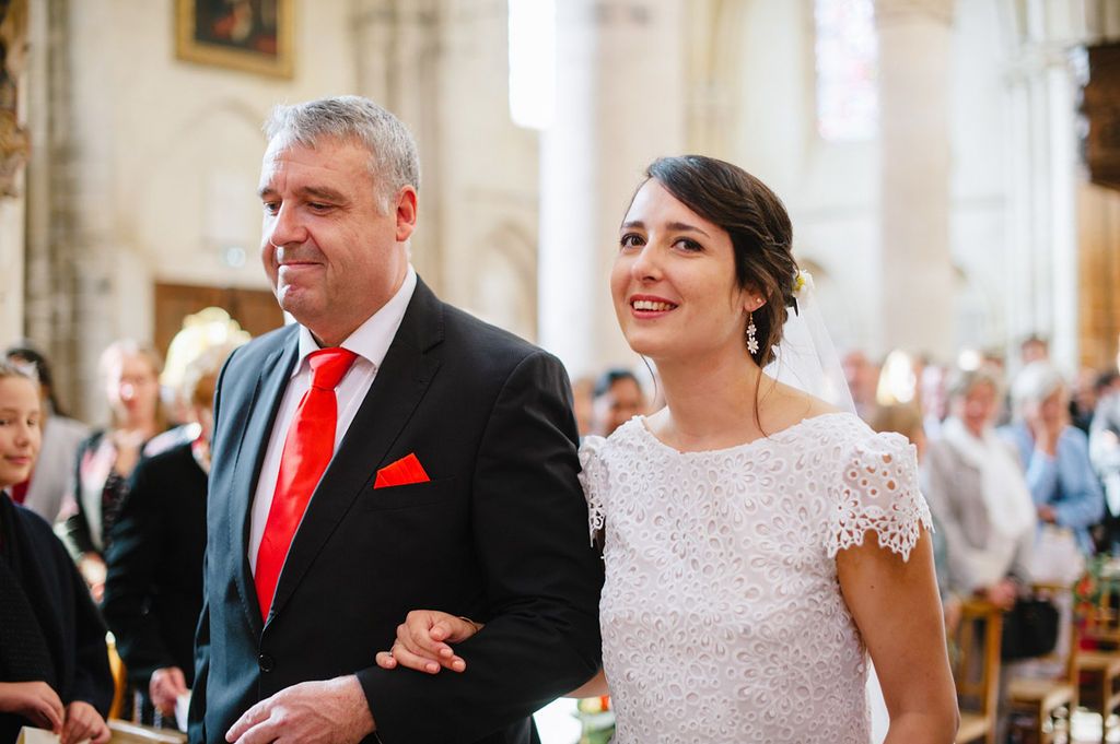 Bride and father sharing a smile while walking down the aisle at church wedding.