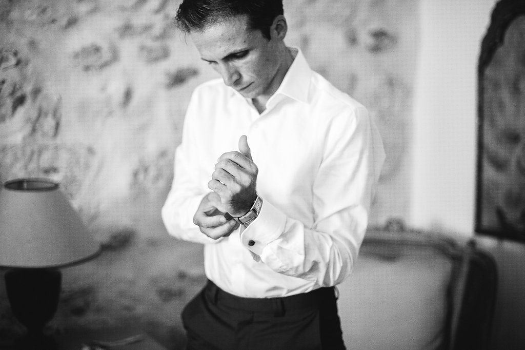 Groom fastening cufflinks on white dress shirt in elegant room before wedding.