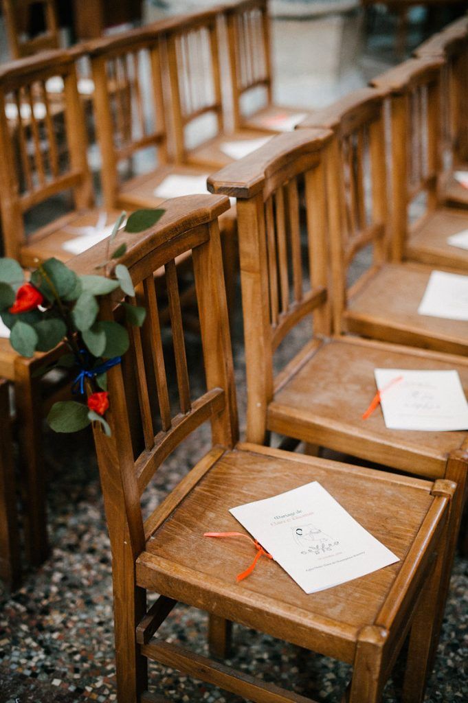 Wooden ceremony chairs with wedding programs and orange ribbon in outdoor venue.