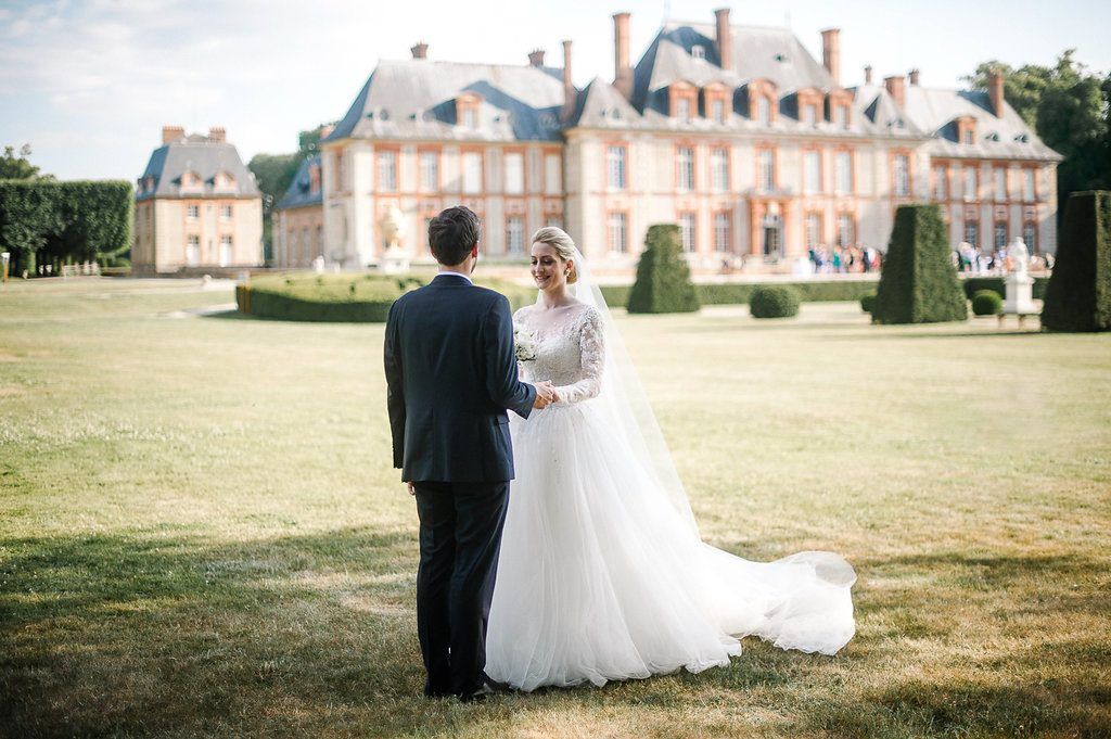 Bride and groom facing each other on lawn before grand French chateau wedding venue.