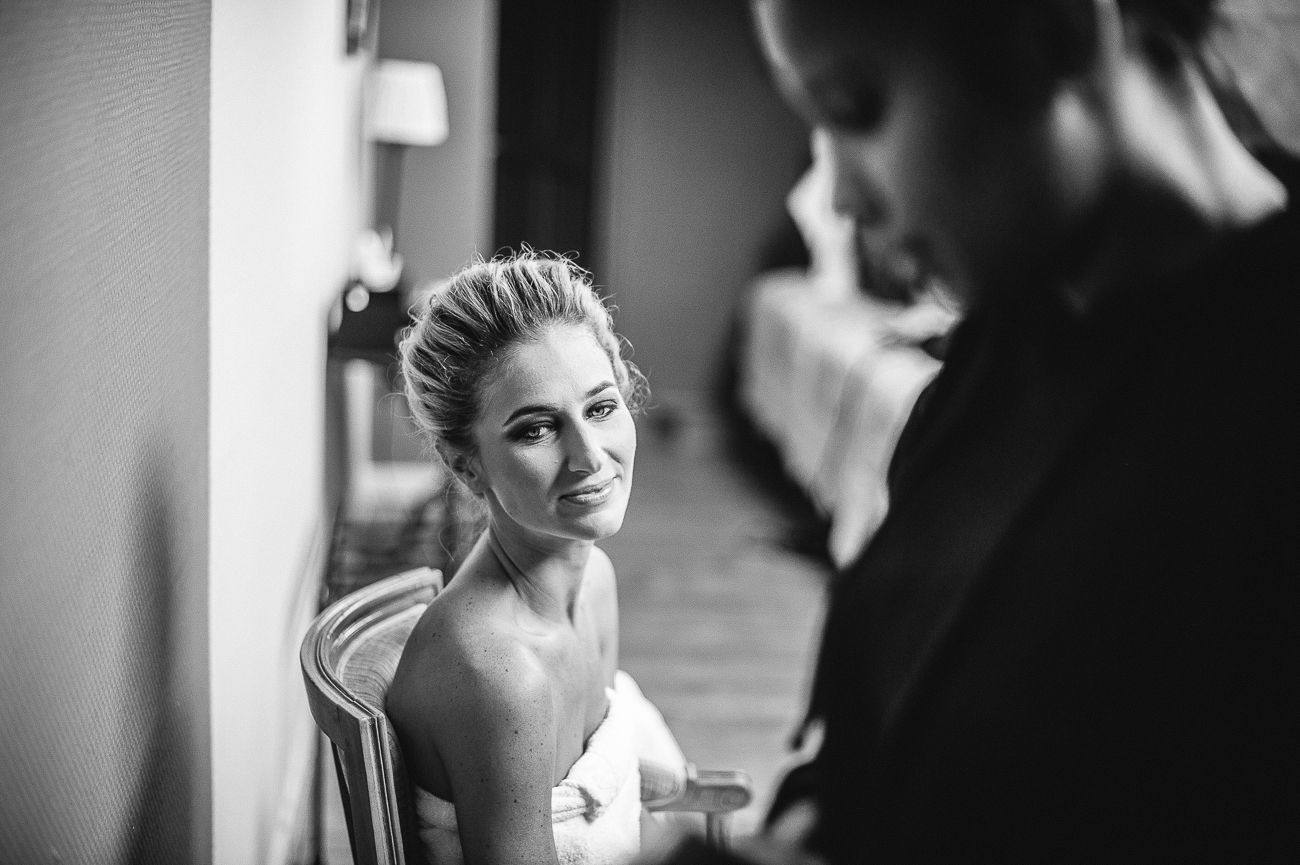 Black and white wedding photo of bride gazing at groom in elegant indoor setting.