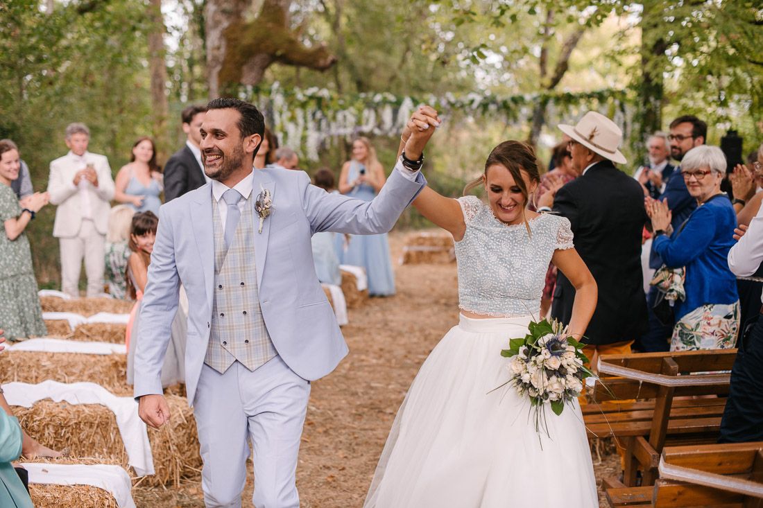 Joyful bride and groom walk back down the aisle after outdoor woodland wedding ceremony.