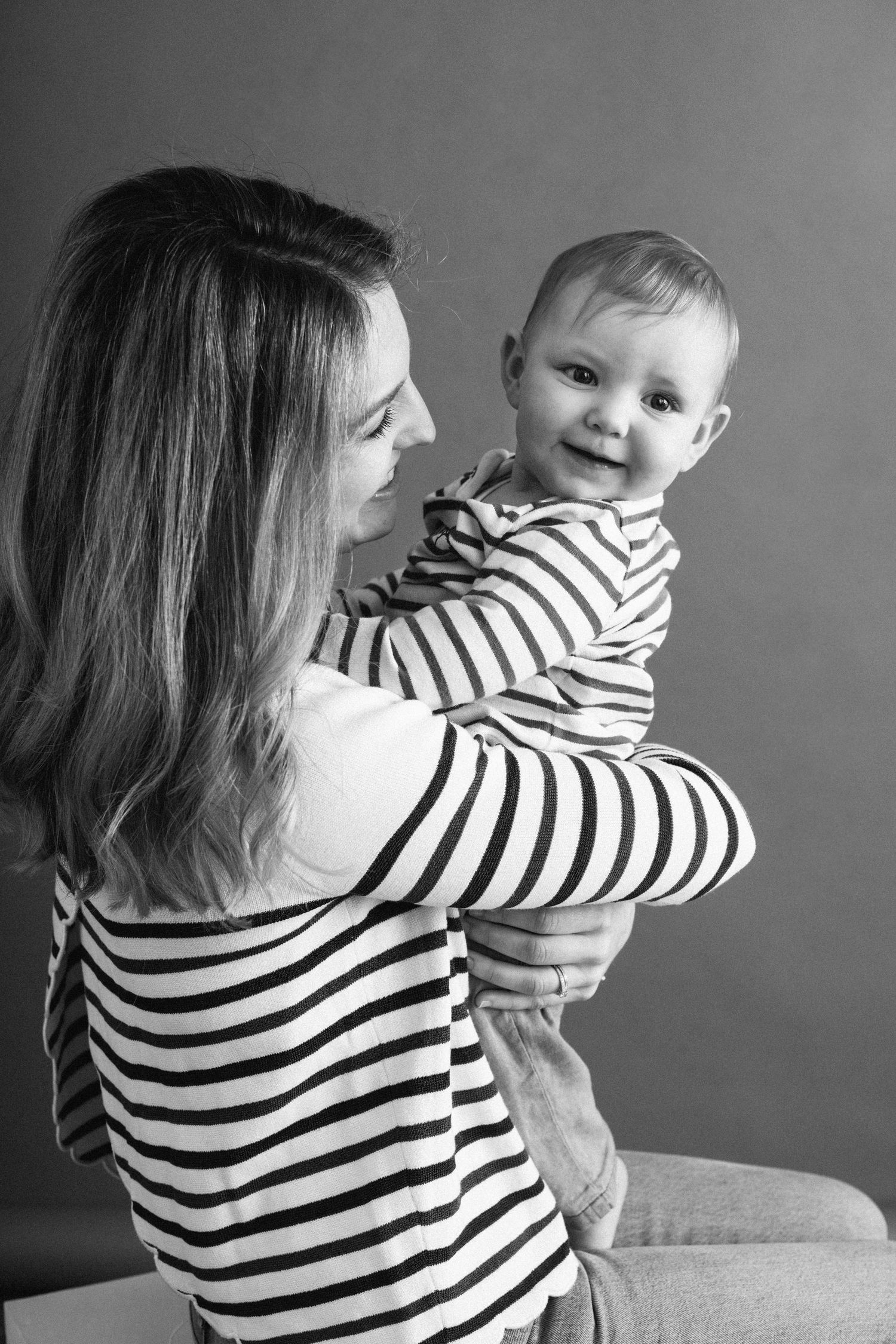 A mother in a striped shirt holds her happy baby in a black and white studio photograph.
