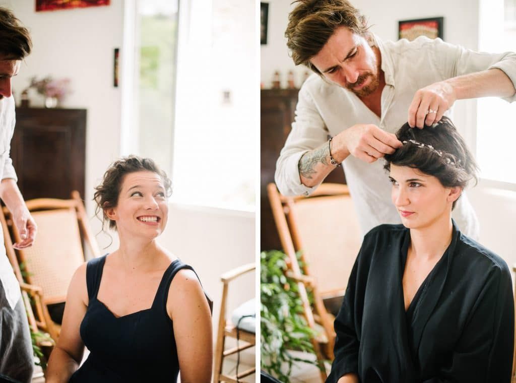 Hairstylist styling bride's hair while smiling woman in black dress watches during wedding preparation.