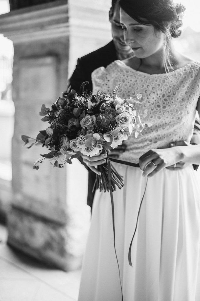 Black and white close-up of bride holding a lush floral bouquet with roses and greenery.