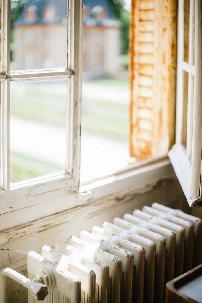 Vintage white window with peeling paint and classic radiator overlooking a garden estate.
