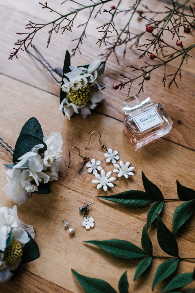 Bridal accessories flat lay with Miss Dior perfume, floral earrings, and boutonnieres.