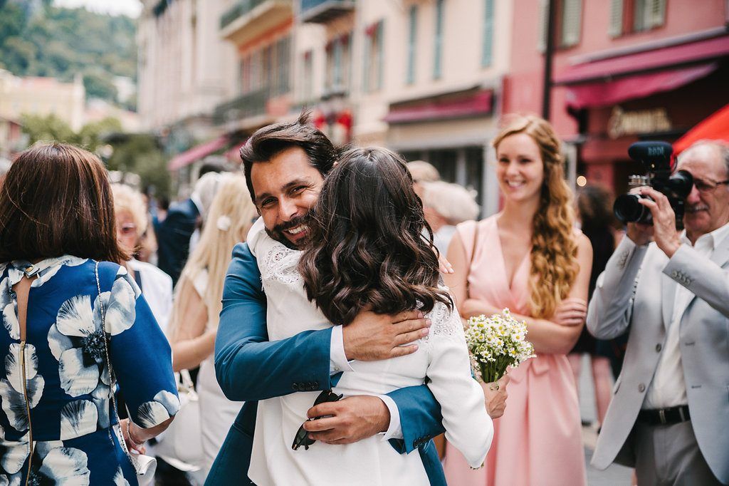 Groom in blue suit embraces a guest warmly outside after a wedding ceremony in Nice.