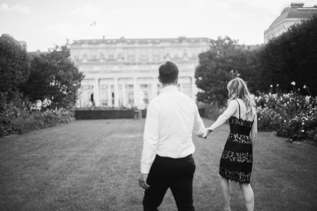 Black and white photo of couple walking hand in hand toward a grand estate building at dusk.