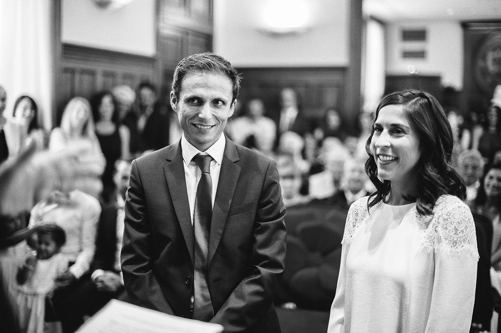 Smiling bride and groom stand together during wedding ceremony in black and white photo.